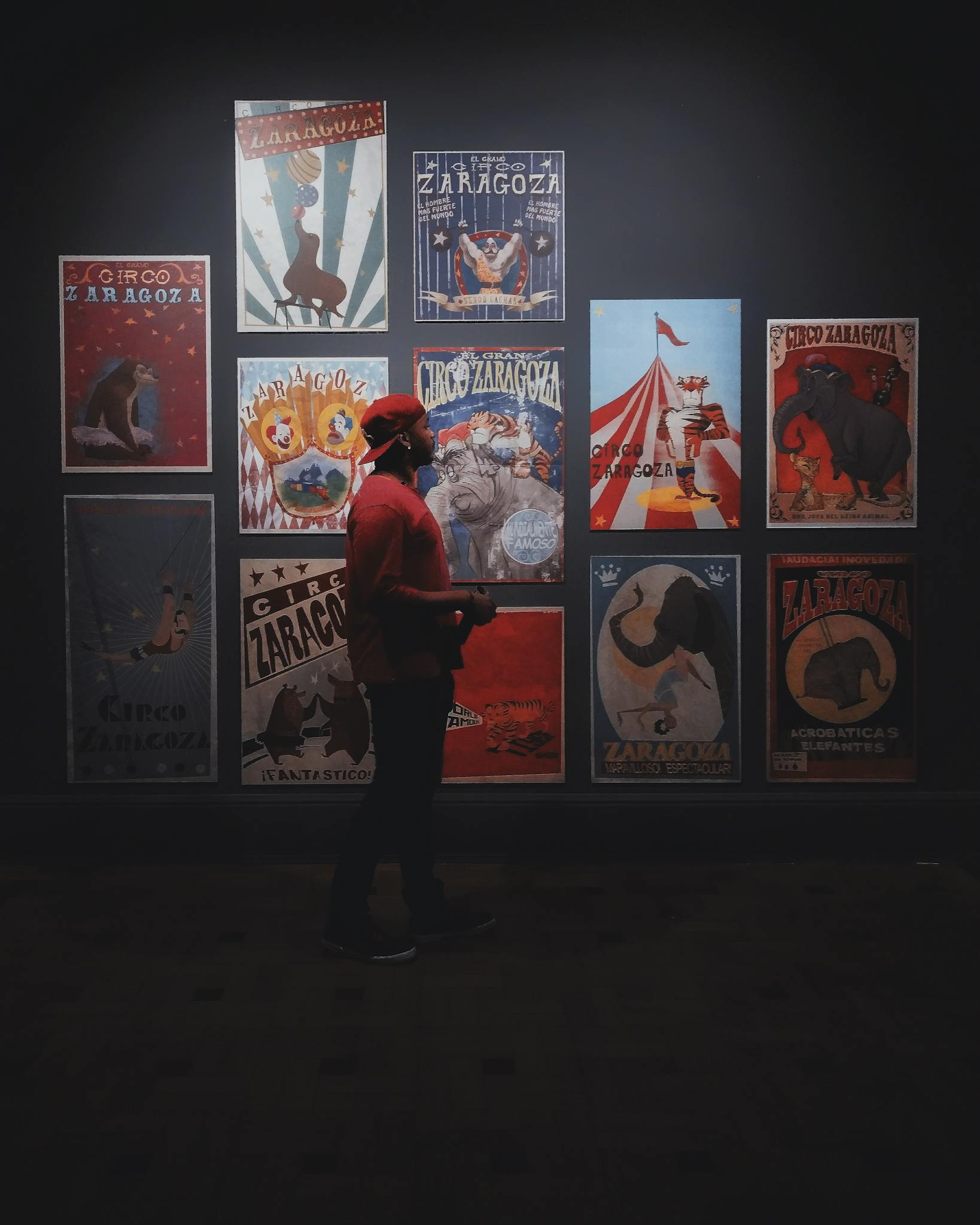 A man in a red cap and t-shirt observes colorful vintage circus posters indoors.