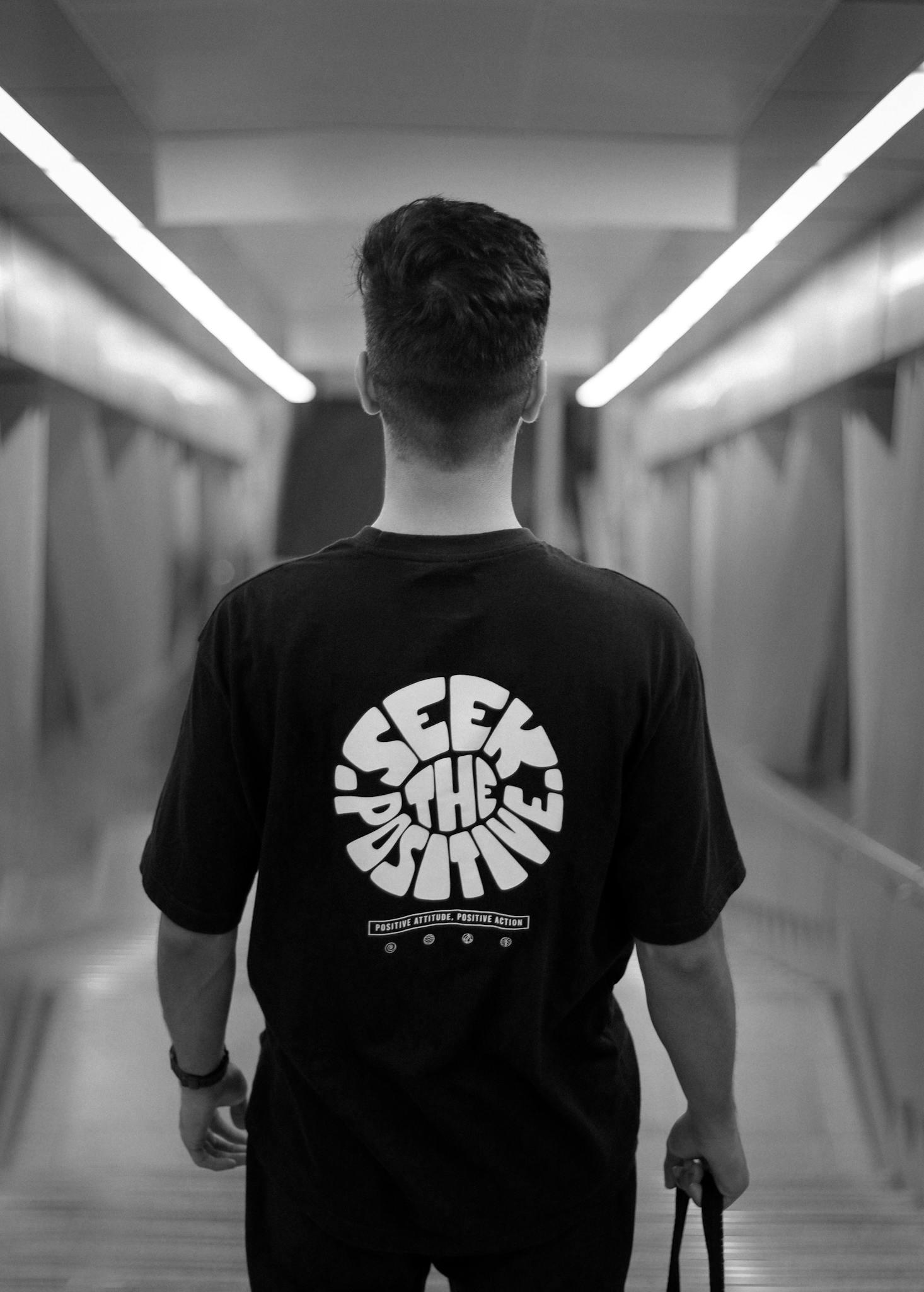 Black and white photo of a man in Dubai walking indoors, wearing a t-shirt with 'Seek the Positive' text.
