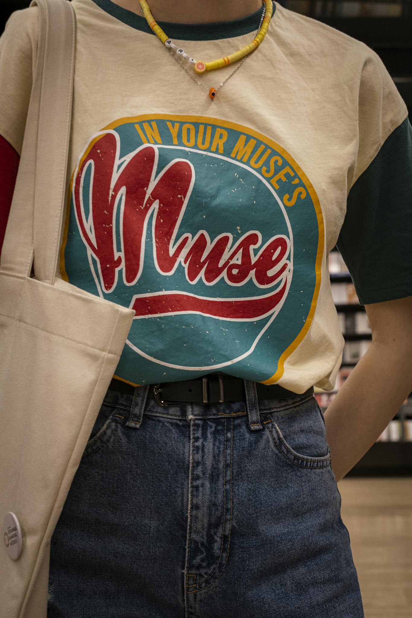 Close-up of a casual outfit featuring a graphic T-shirt, jeans, tote bag, and necklace.
