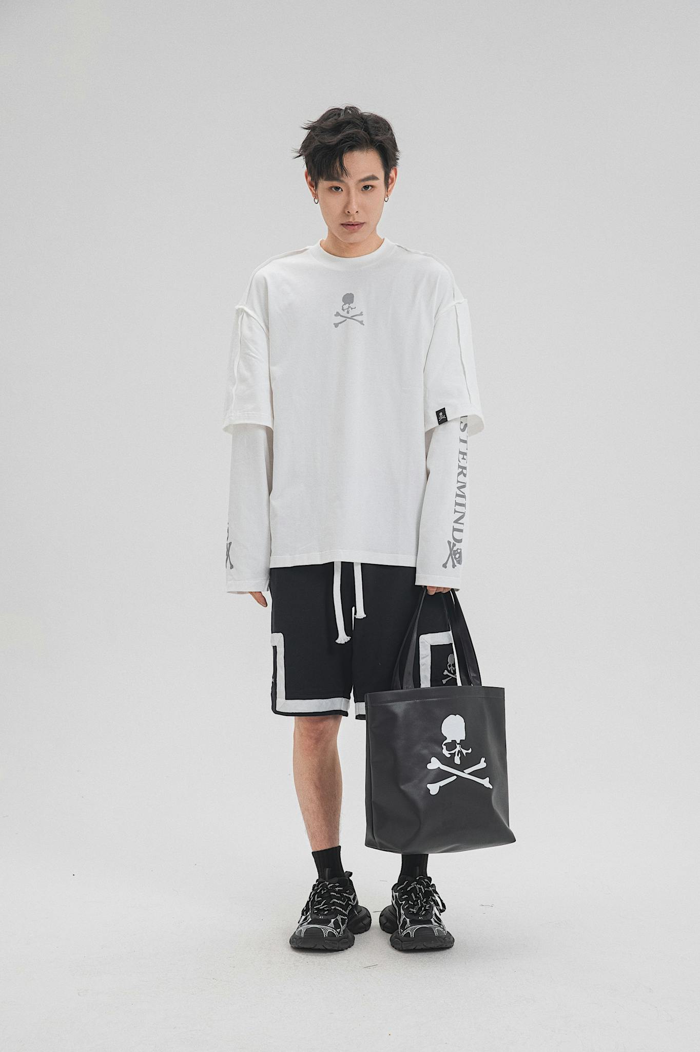Fashionable man posing with monochrome sportswear and branded tote in studio.