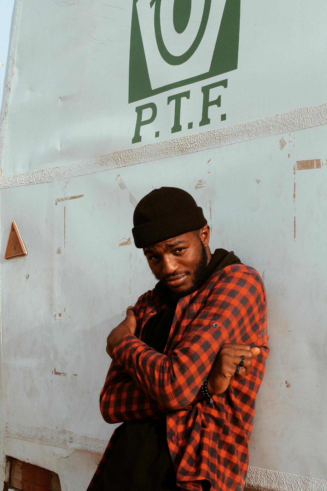 Portrait of a stylish man in a checkered shirt posing confidently against a wall with logo.