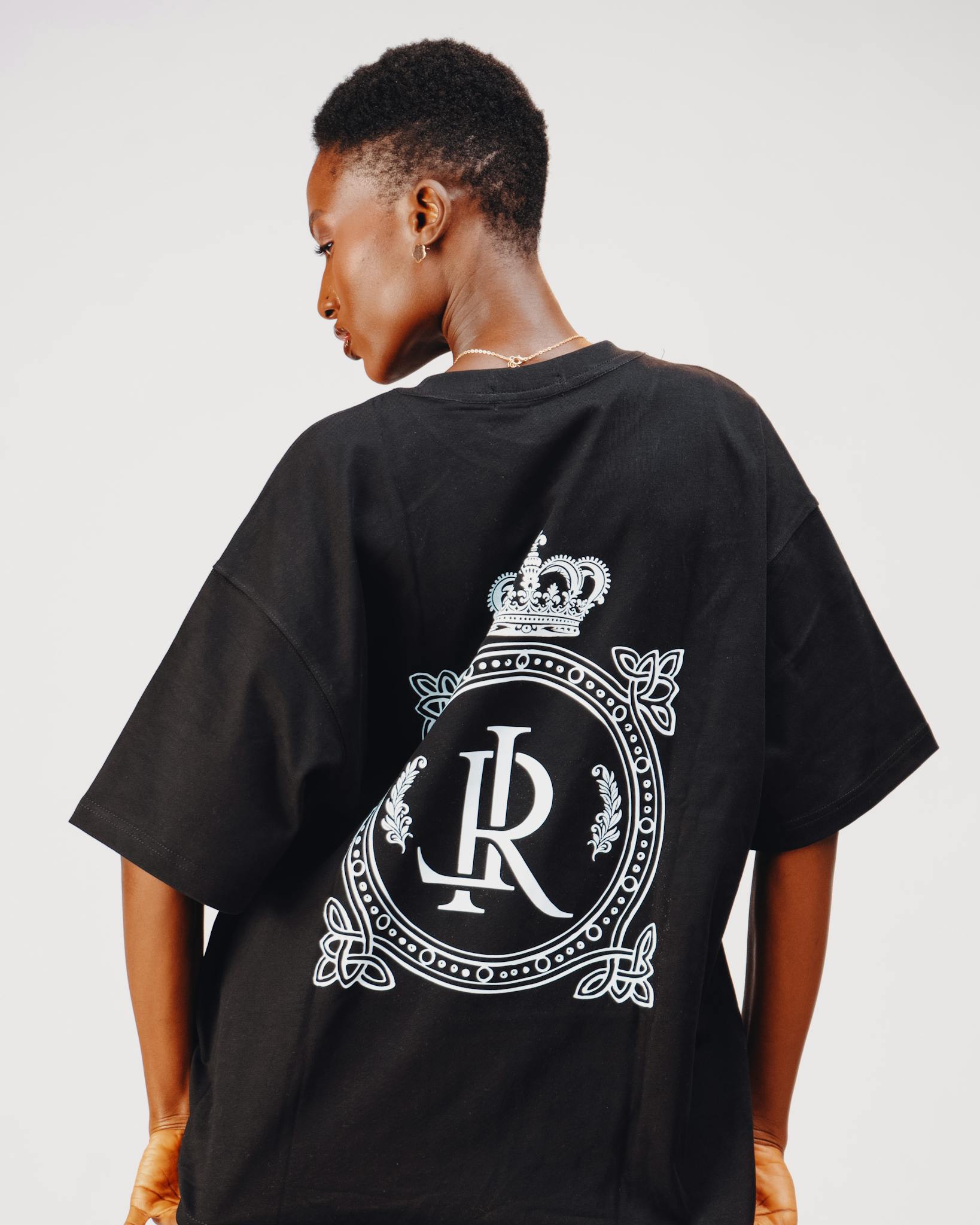 Stylish black t-shirt featuring a decorative royal emblem, worn by young adult.